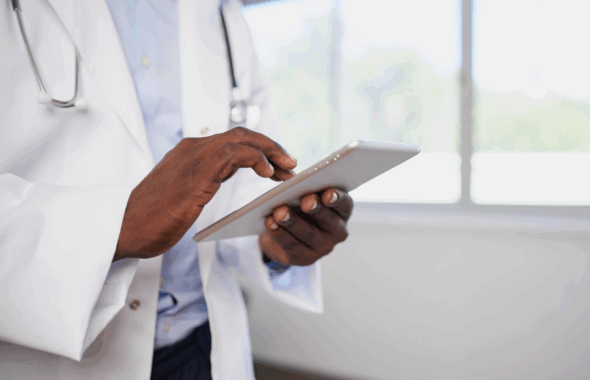 Arzt in weißem Kittel nutzt Tablet-PC in heller Praxis.