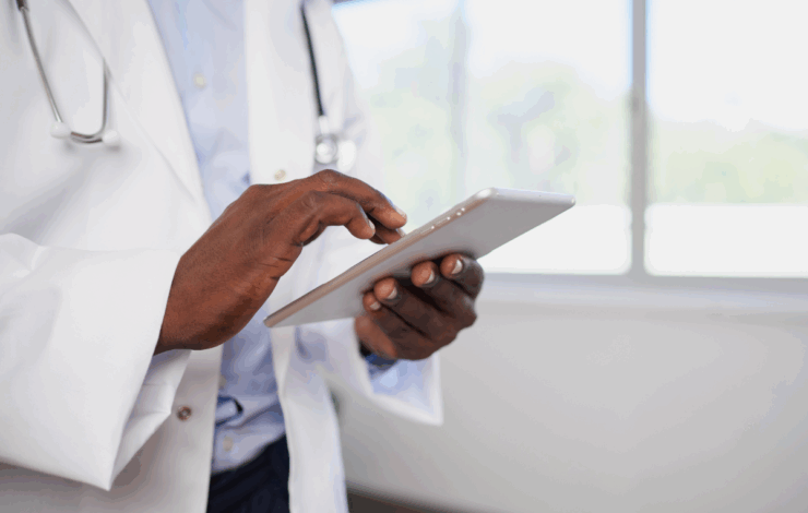 Arzt in weißem Kittel nutzt Tablet-PC in heller Praxis.