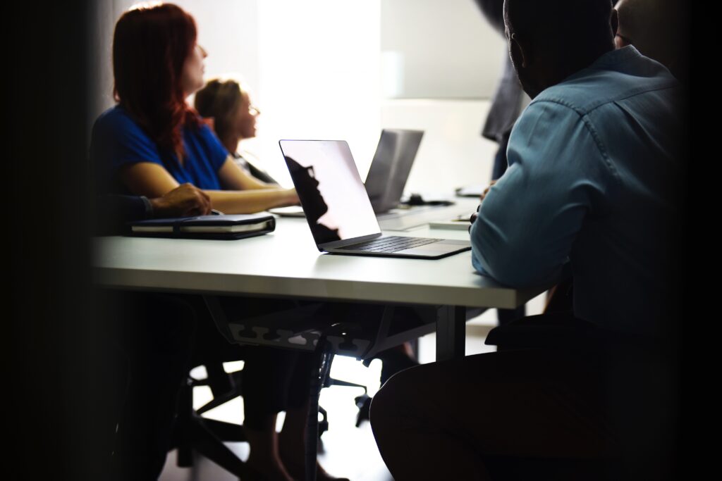 Personen sitzen mit Laptops an einem nicht vollständig ausgeleuchteten Tisch