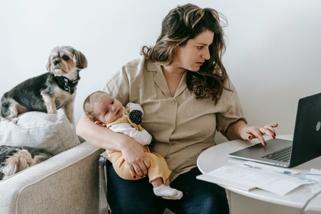 Mutter sitzt mit Baby auf dem Arm vor einem Laptop