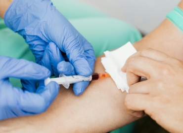 Blutentnahme am Arm mit Spritze durch medizinisches Fachpersonal in Einmalhandschuhen